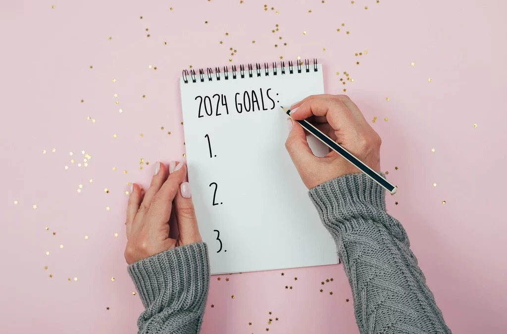 La imagen muestra las manos de una mujer escribiendo en una libreta las metas para el nuevo año.